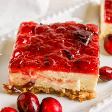 A cheesecake bar with a crumb crust and cranberry topping, garnished with whole cranberries.