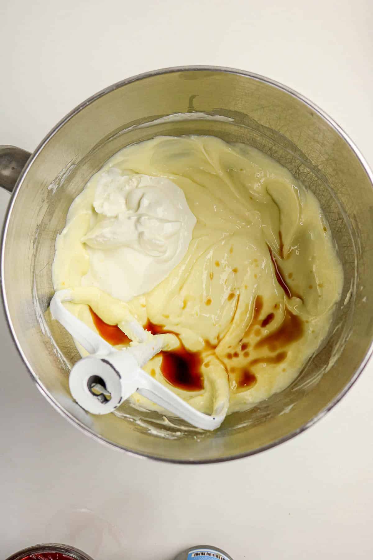 Stand mixer bowl with creamy batter, sour cream, and vanilla extract on top, ready to be mixed.