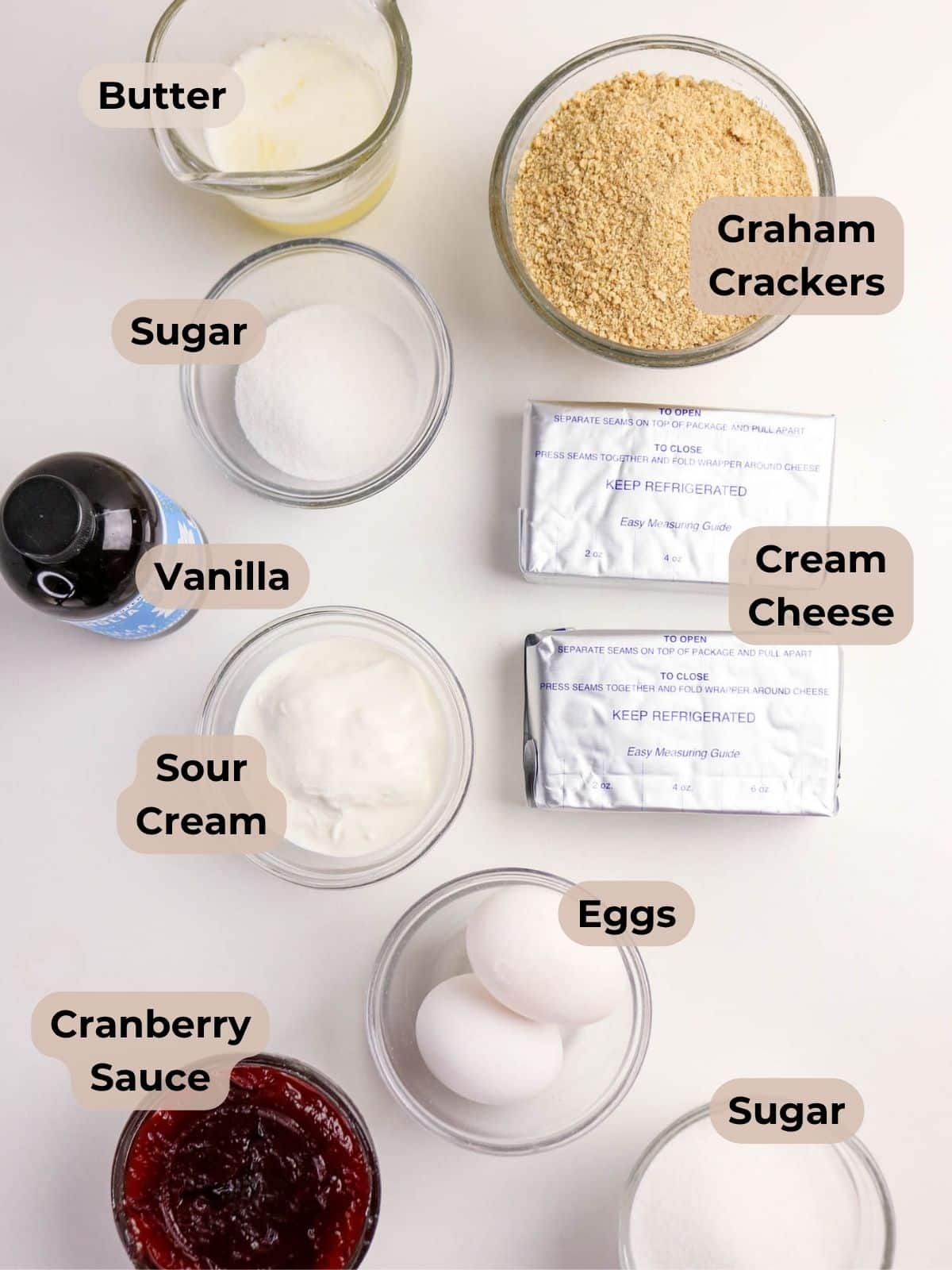 Labeled cheesecake ingredients-graham crackers, cream cheese, butter, sugar, vanilla, eggs, sour cream, cranberry sauce.
