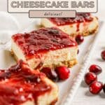 Three cranberry cheesecake bars with cranberry topping on a white tray, surrounded by fresh cranberries.