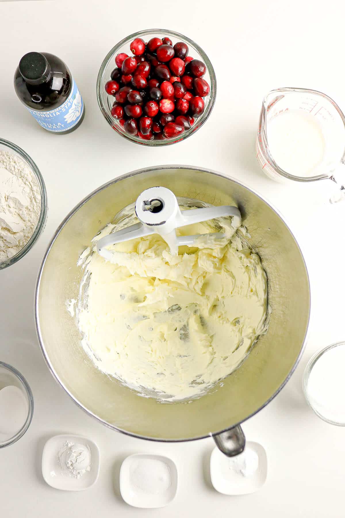 Overhead view of a mixing bowl with creamed butter, surrounded by baking ingredients like cranberries and flour.