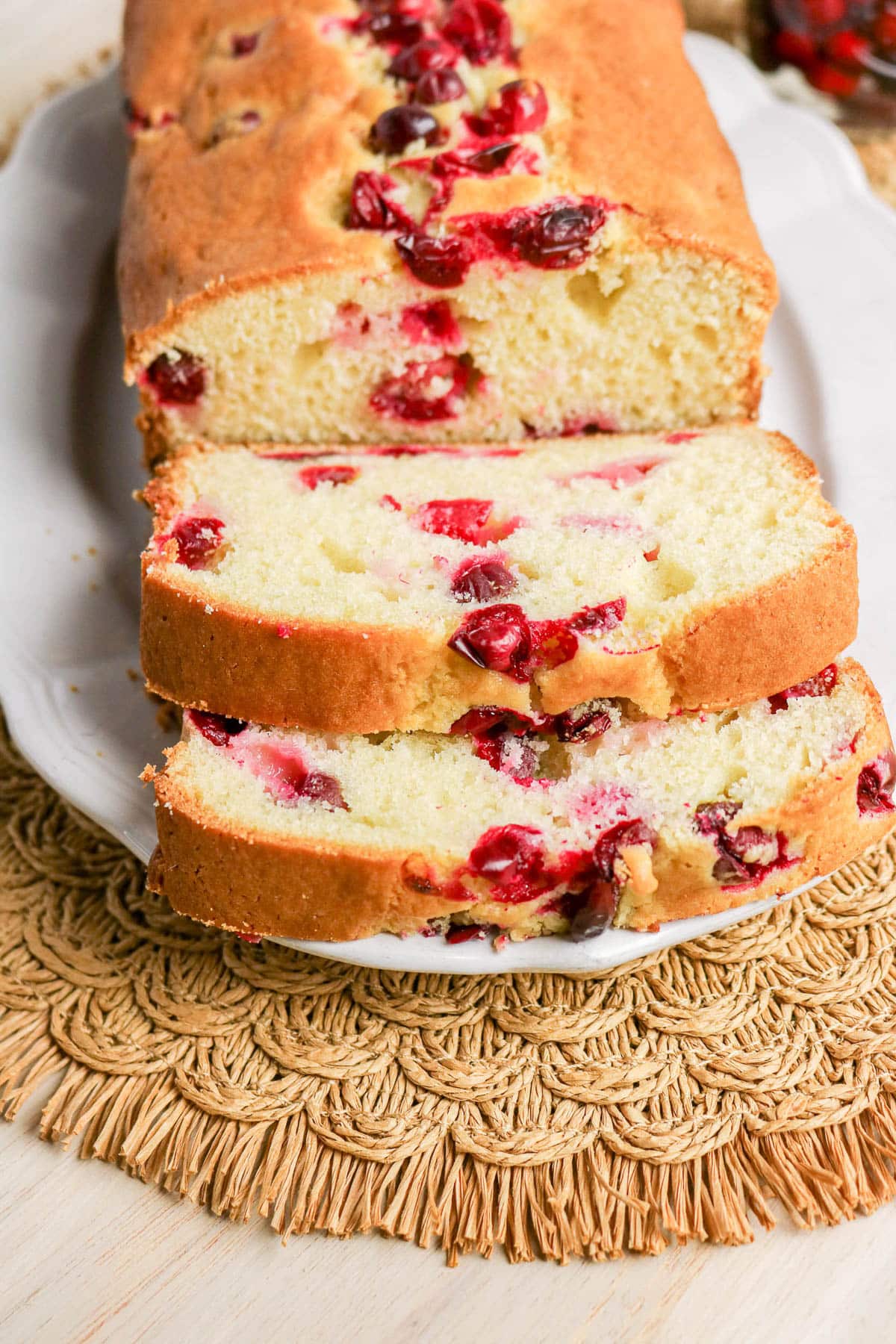 A loaf of cranberry bread on a white plate, with two slices cut and cranberries visible inside.