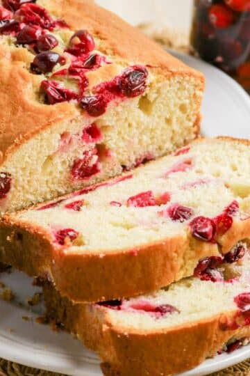 Sliced cranberry bread loaf on a white plate, showing cranberries inside and on top of the bread.