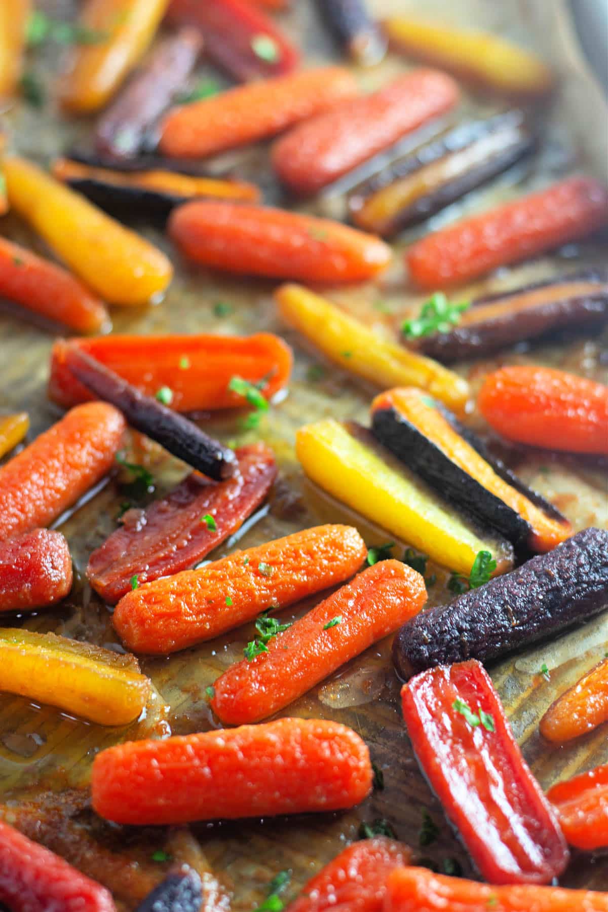 Colorful roasted carrots on a baking sheet, garnished with chopped herbs.