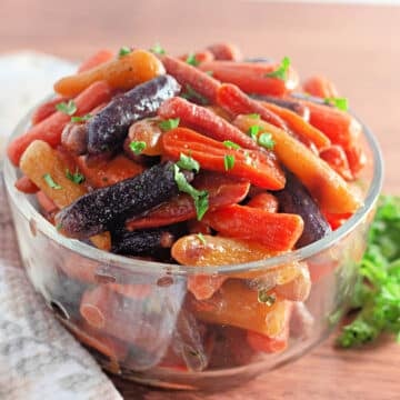 A glass bowl filled with colorful glazed baby carrots garnished with chopped parsley.