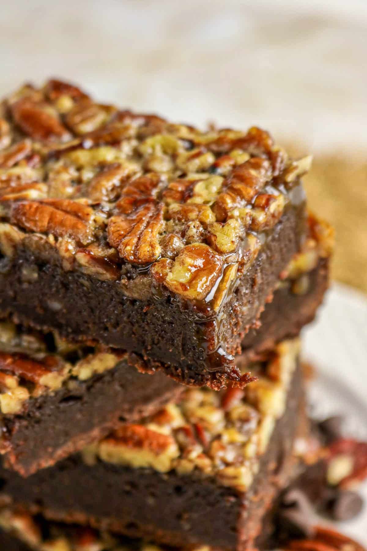 Close-up of stacked brownies topped with chopped pecans and a glossy glaze.