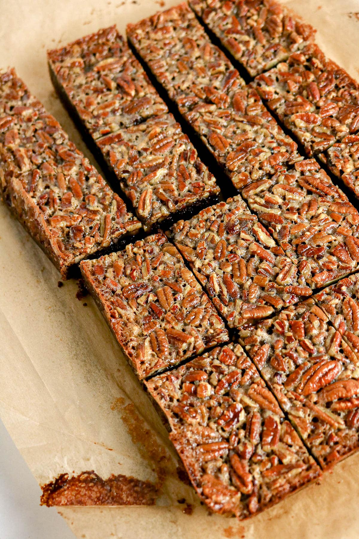 Sliced pecan bars on parchment paper, showing a nutty, golden-brown top and chewy texture.