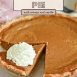 A pumpkin pie with a slice missing, topped with whipped cream, on a glass pie dish.