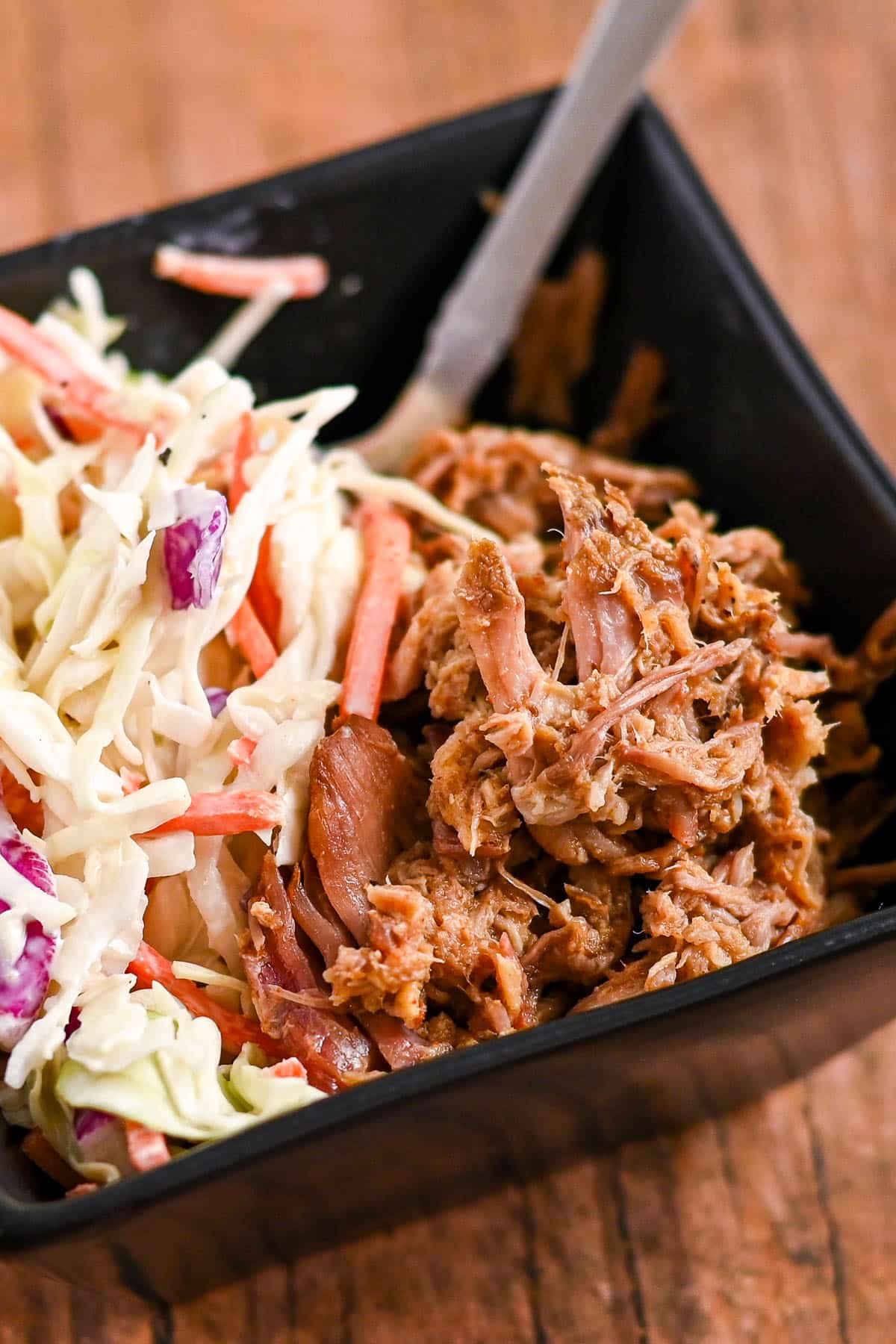 Shredded barbecue pork and coleslaw served in a black square bowl with a fork.