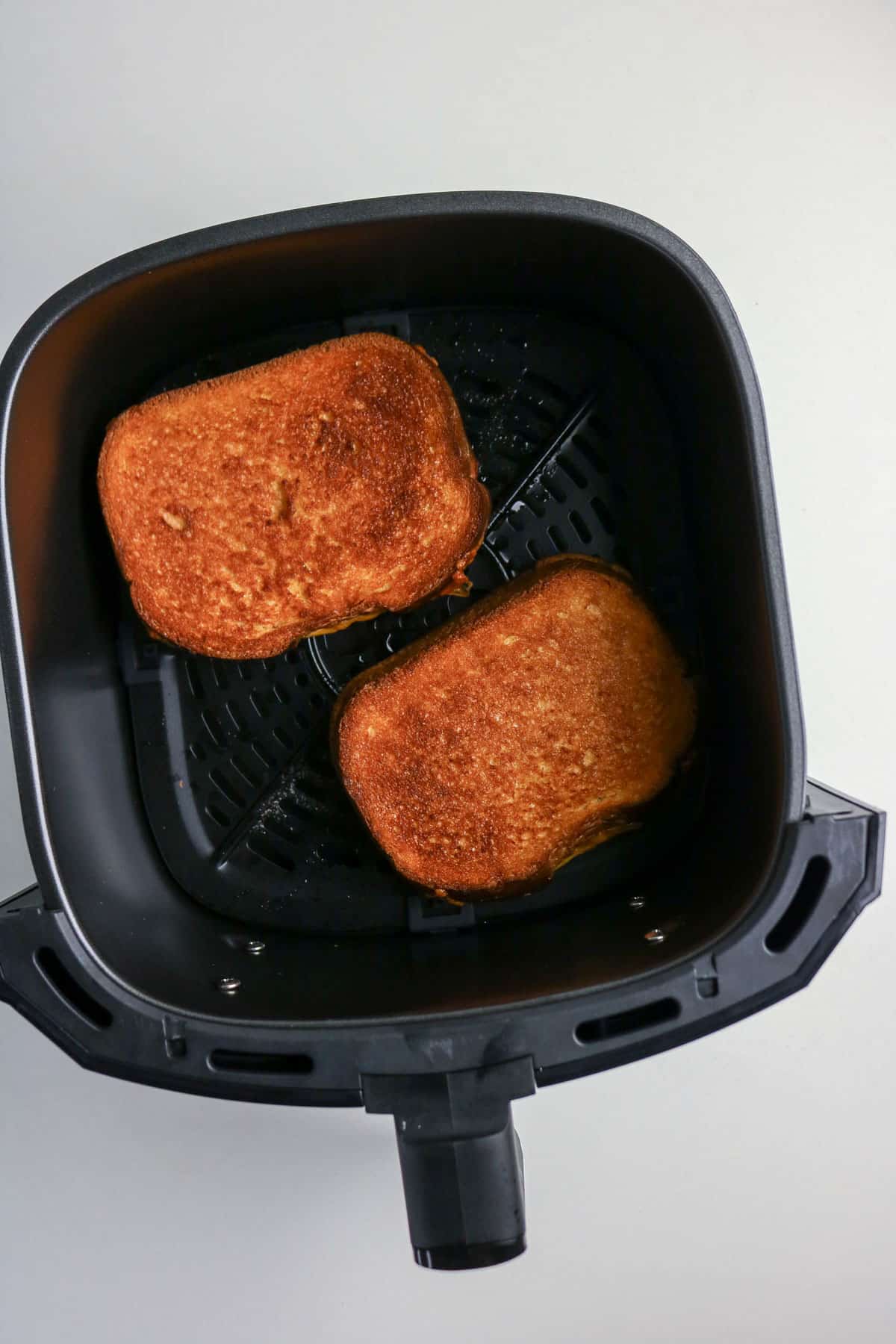 Two slices of toasted bread in an air fryer basket on a white surface.