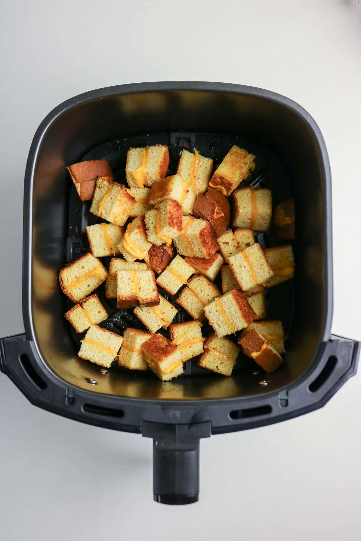 Cubed bread pieces filled with cheese inside an air fryer basket, being toasted to make croutons.