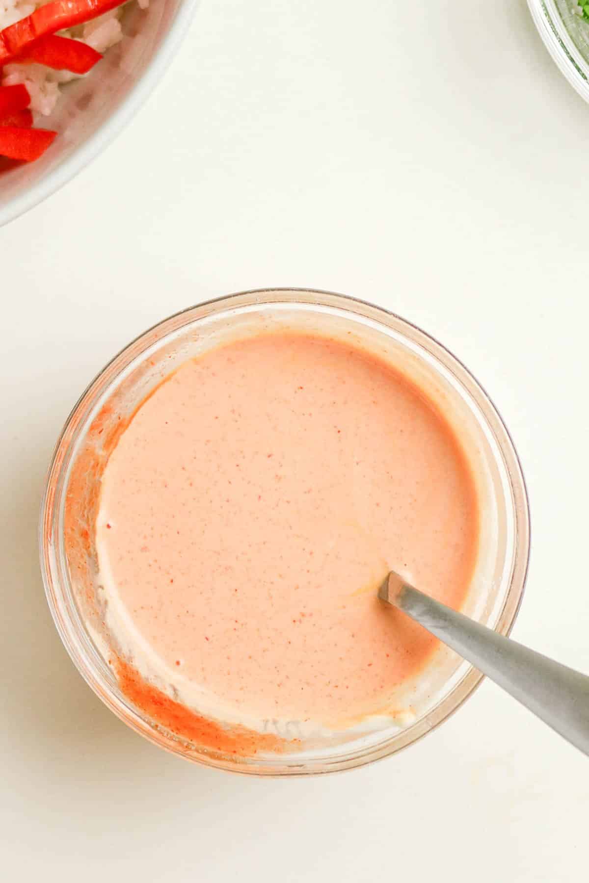 A bowl of creamy pink sauce with a spoon in it, photographed from above on a white surface.