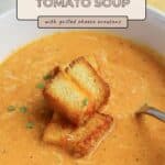 Bowl of Roasted Tomato Soup topped with Grilled Cheese Croutons and a sprinkle of herbs.