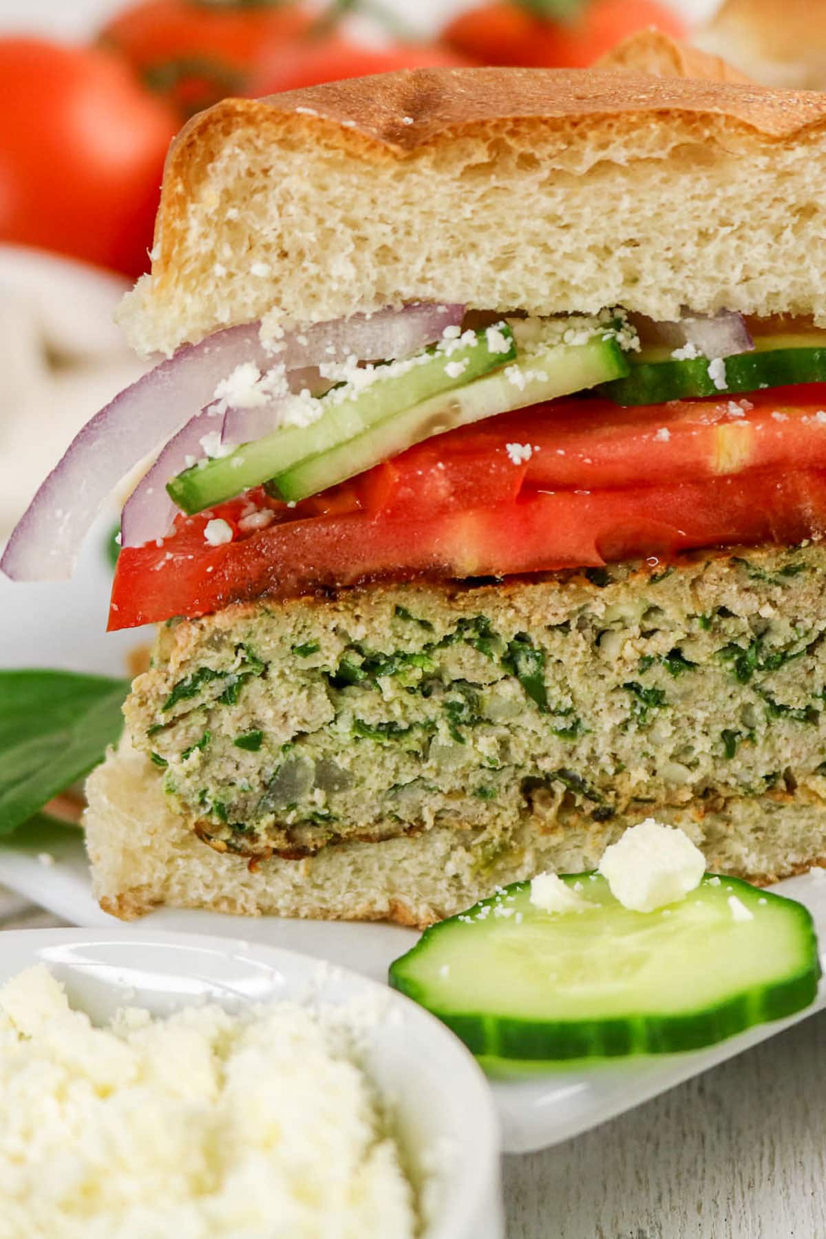 Close-up of a feta and spinach ground turkey burger, tomato, cucumber, red onion, feta, and thick bread.