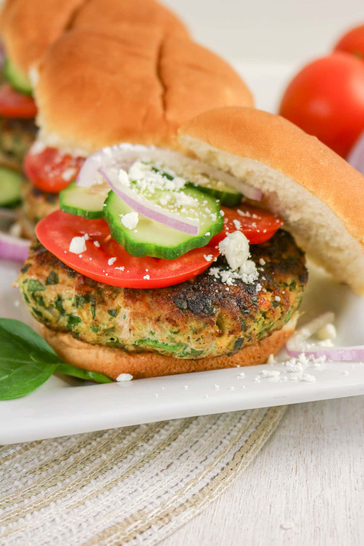 A veggie burger with tomato, cucumber, red onion, and feta cheese on a bun, served on a white plate.