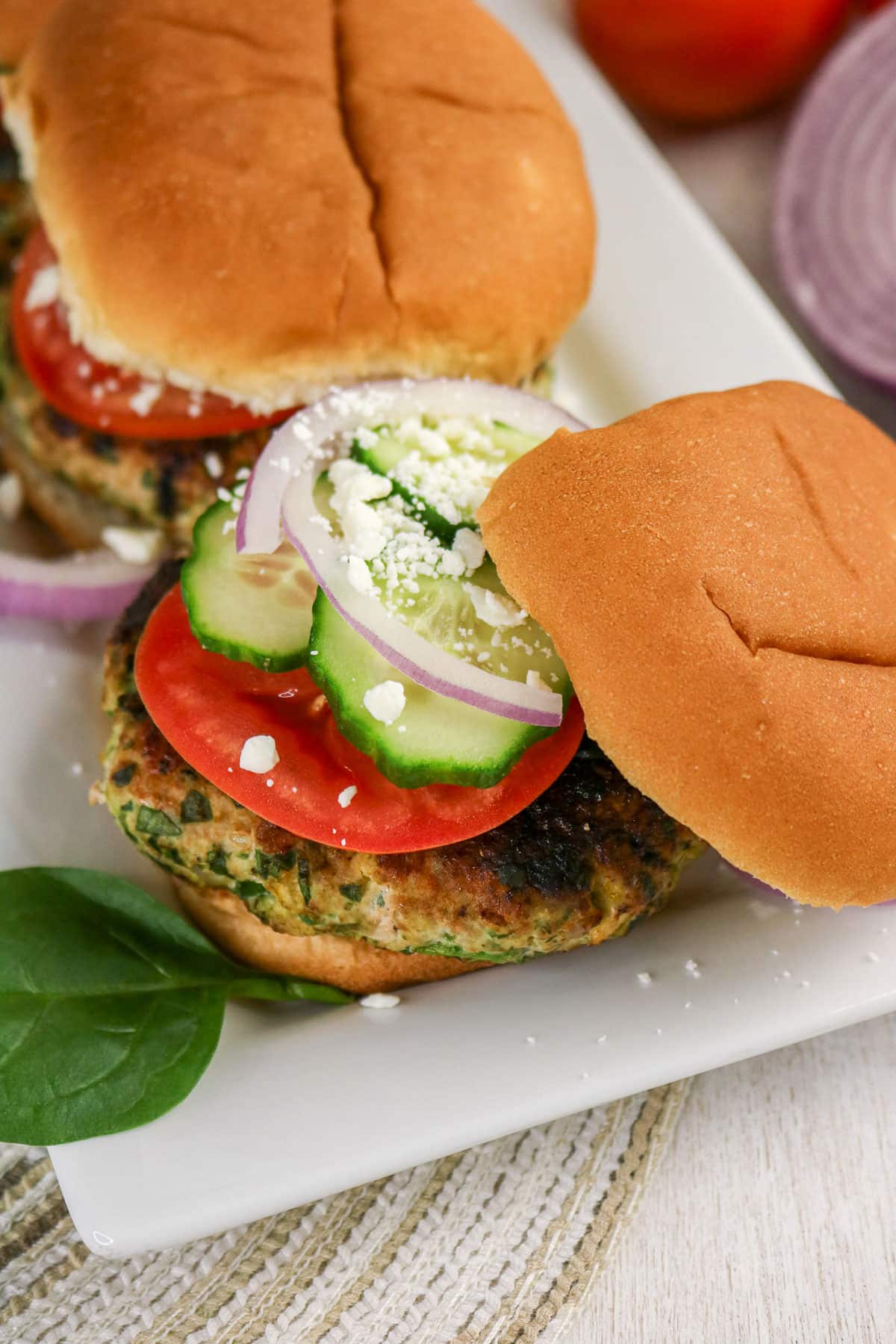 Veggie burger topped with tomato, cucumber, red onion, and feta cheese on a white plate.