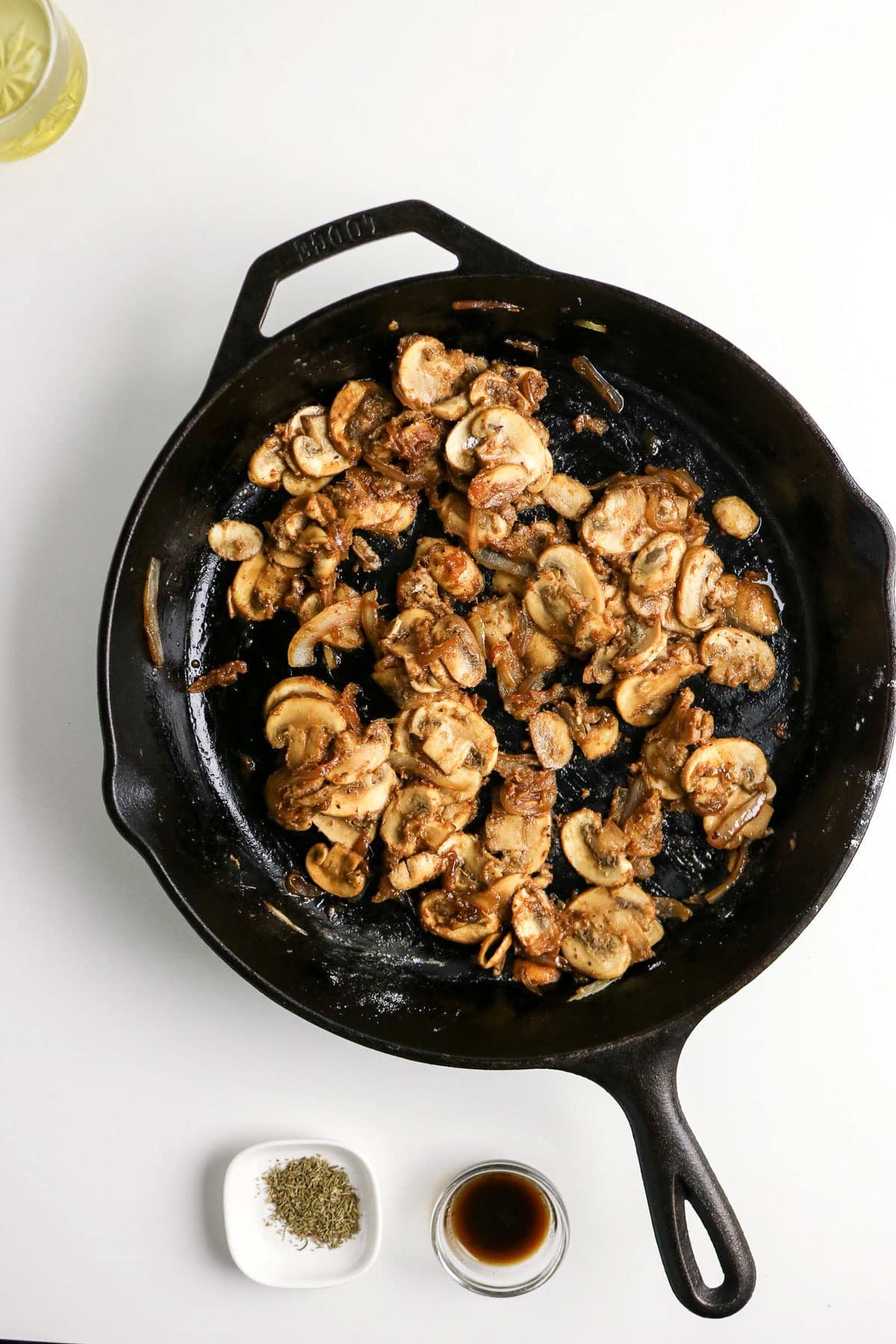 Sautéed mushrooms in a cast iron skillet with small bowls of salt, pepper, and soy sauce on the side.