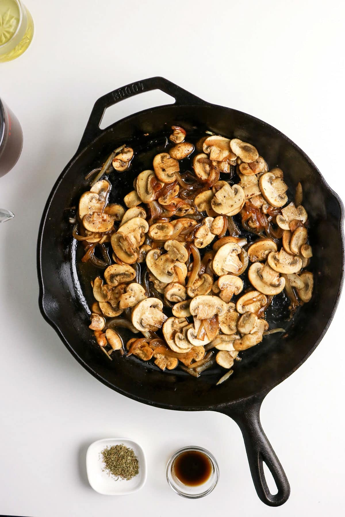 Sliced mushrooms and onions sautéing in a black cast iron skillet, with seasonings and sauce nearby.