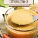 A bowl of Miso Sesame Dressing with a spoon, topped with sesame seeds, sits next to freshly sliced vegetables.