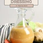 A glass jug of Miso Sesame Dressing sits beside sliced carrots, ginger, and lettuce on a striped cloth.