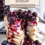 Stack of pancakes topped with blueberry syrup and fresh blueberries on a white plate with a fork.