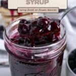 A spoon scoops blueberry syrup from a glass jar, with text overlay: "Blueberry Syrup using fresh or frozen berries.