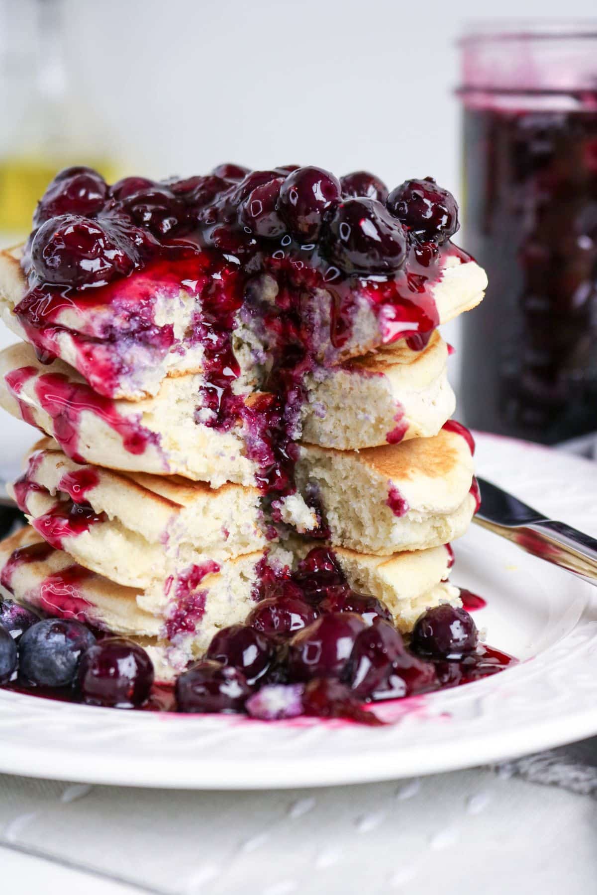 A stack of pancakes topped with blueberry sauce on a white plate, with blueberries on the side.