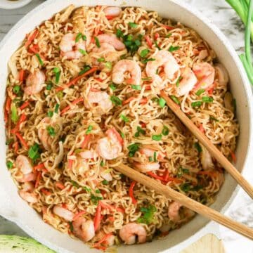A bowl of Shrimp Yakisoba stir-fry noodles with chopped green onions, red peppers, and chopsticks on top.