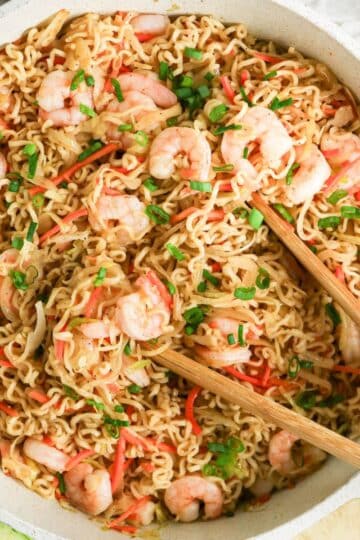 A bowl of Shrimp Yakisoba stir-fry noodles with chopped green onions, red peppers, and chopsticks on top.
