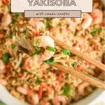 Chopsticks holding shrimp yakisoba with ramen noodles above a pan filled with the dish, garnished with green onions.
