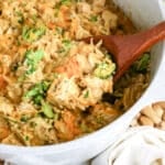 A pot of cheesy chicken, broccoli, and rice casserole with a wooden spoon scooping out a portion.