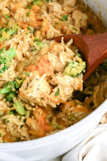 A pot of cheesy chicken, broccoli, and rice casserole with a wooden spoon scooping out a portion.