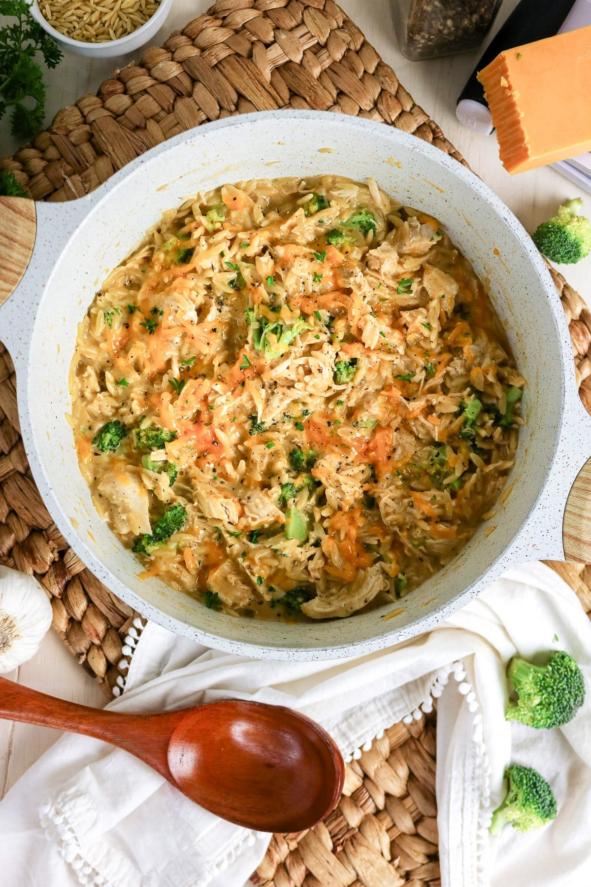 A creamy chicken, broccoli, and rice casserole in a white pot, topped with shredded cheese and herbs.