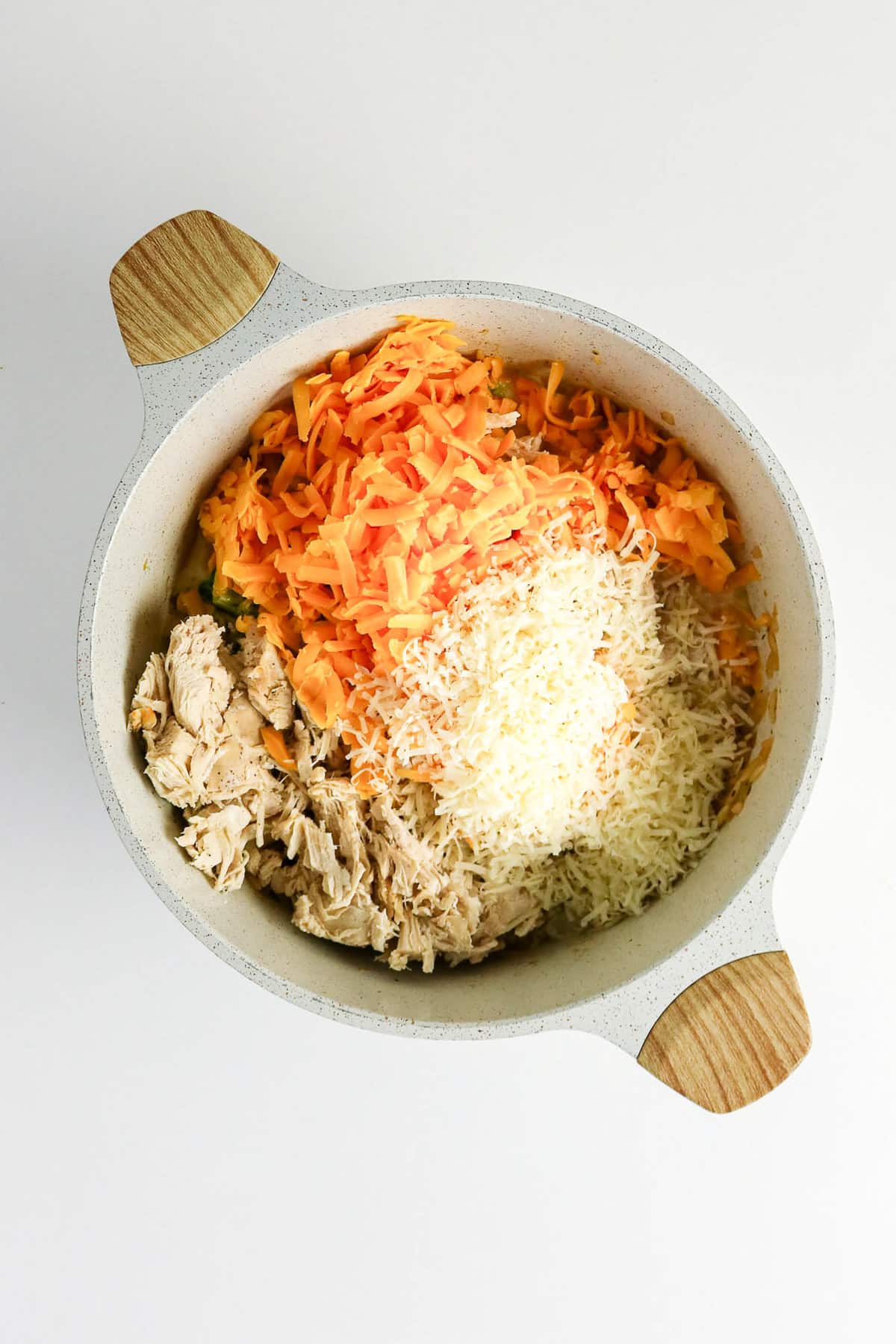 A bowl with shredded chicken, grated carrots, and shredded cheese on a white background.