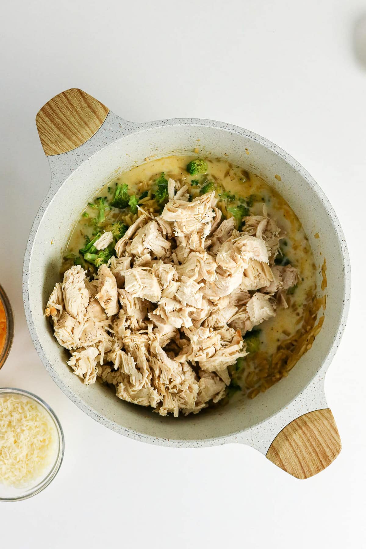 A white pot with shredded chicken, broccoli, and sauce mixture, seen from above on a white surface.