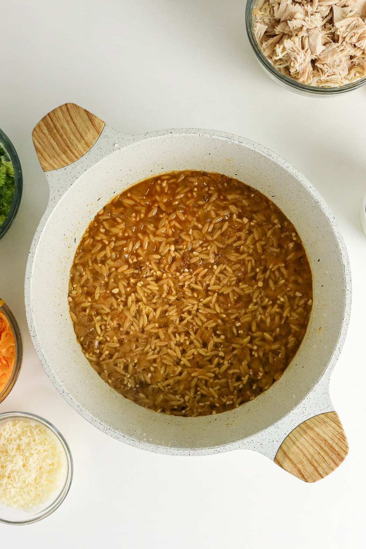 A pot of cooked rice in broth, surrounded by bowls of shredded chicken, cheese, and vegetables.