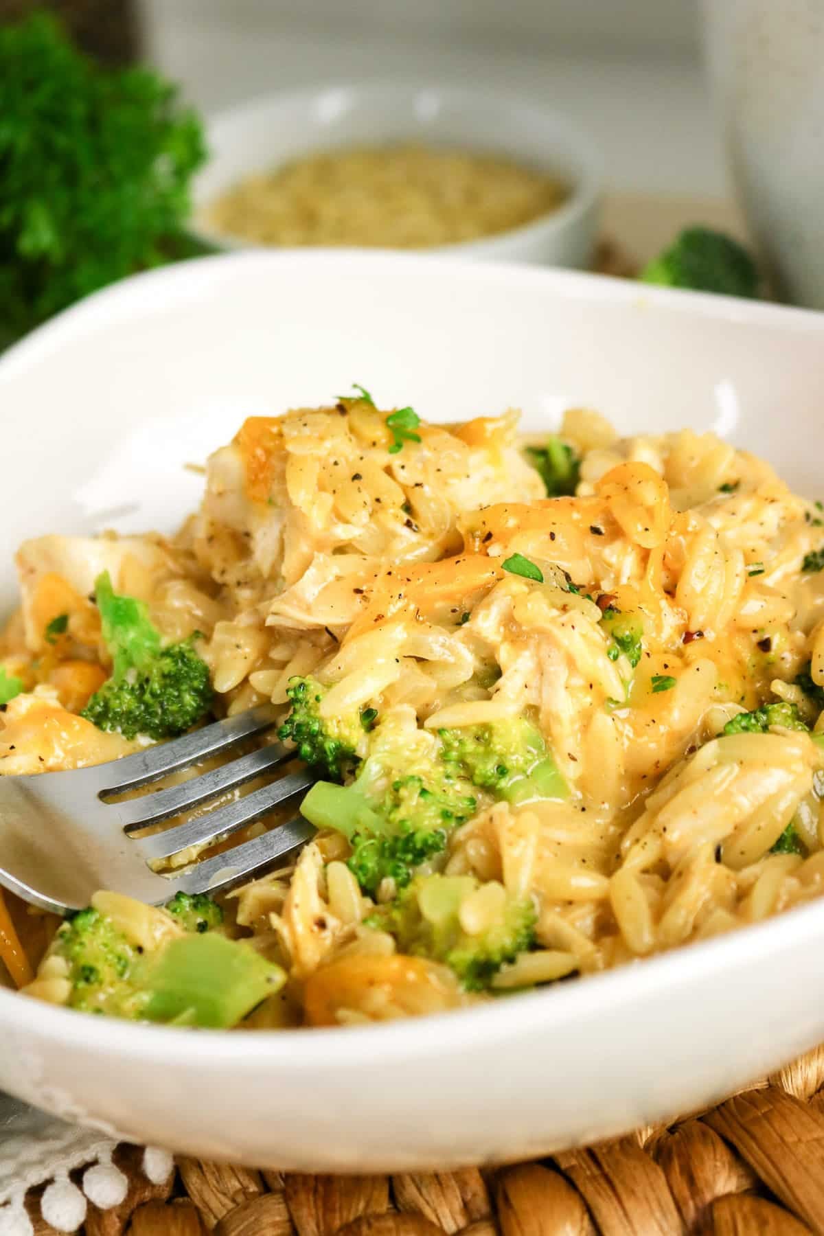 A close-up of creamy orzo pasta with broccoli and cheese in a white bowl, with a fork resting inside.