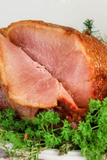 A sliced glazed ham on a plate, garnished with fresh green herbs.