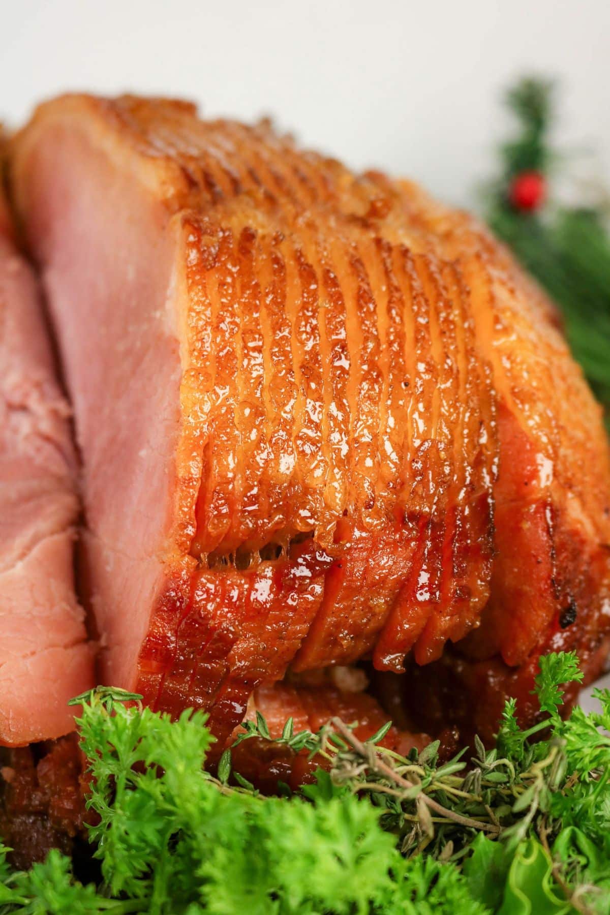 Close-up of glazed, sliced ham with crispy edges, garnished with fresh herbs and greenery.