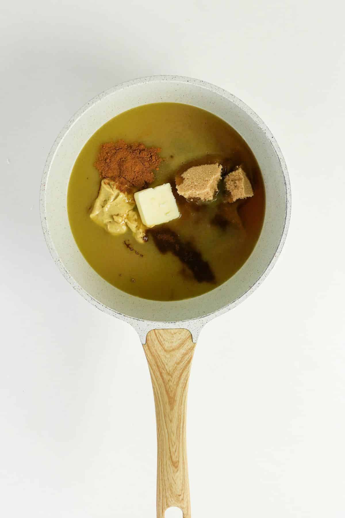 A white saucepan with butter, brown sugar, spices, and other ingredients ready to be mixed.