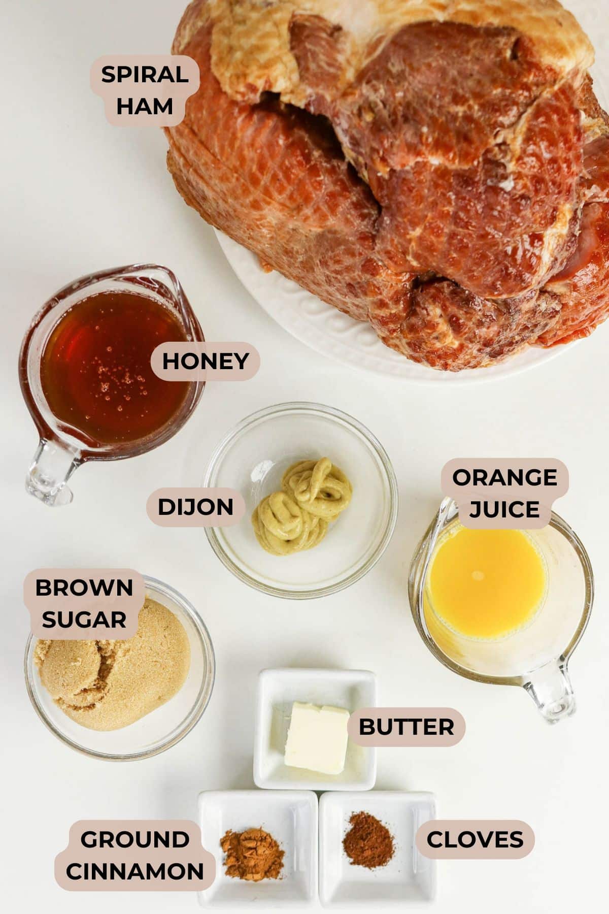 Spiral ham on a plate with bowls of honey, Dijon, brown sugar, orange juice, butter, cinnamon, and cloves.