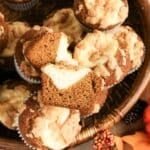 Pumpkin muffins with cream cheese filling and crumb topping arranged in a basket with autumn decorations.
