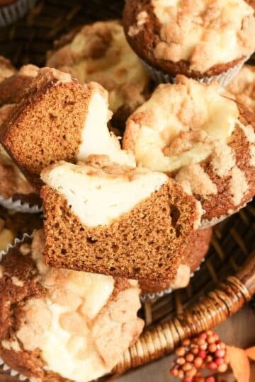 Pumpkin muffins with cream cheese filling and crumb topping arranged in a basket with autumn decorations.
