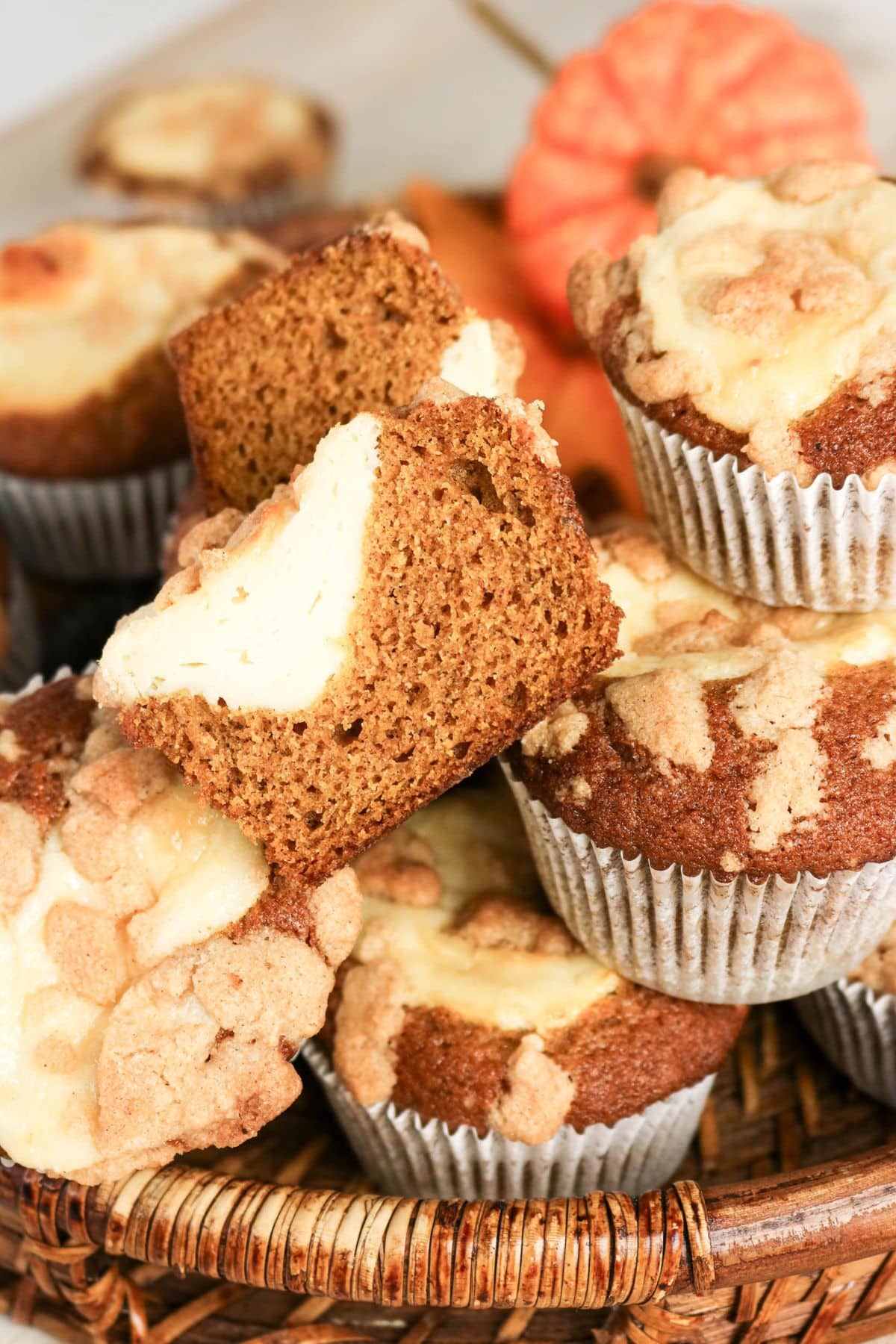 Pumpkin cream cheese muffins in a basket, one muffin cut in half to show creamy filling.