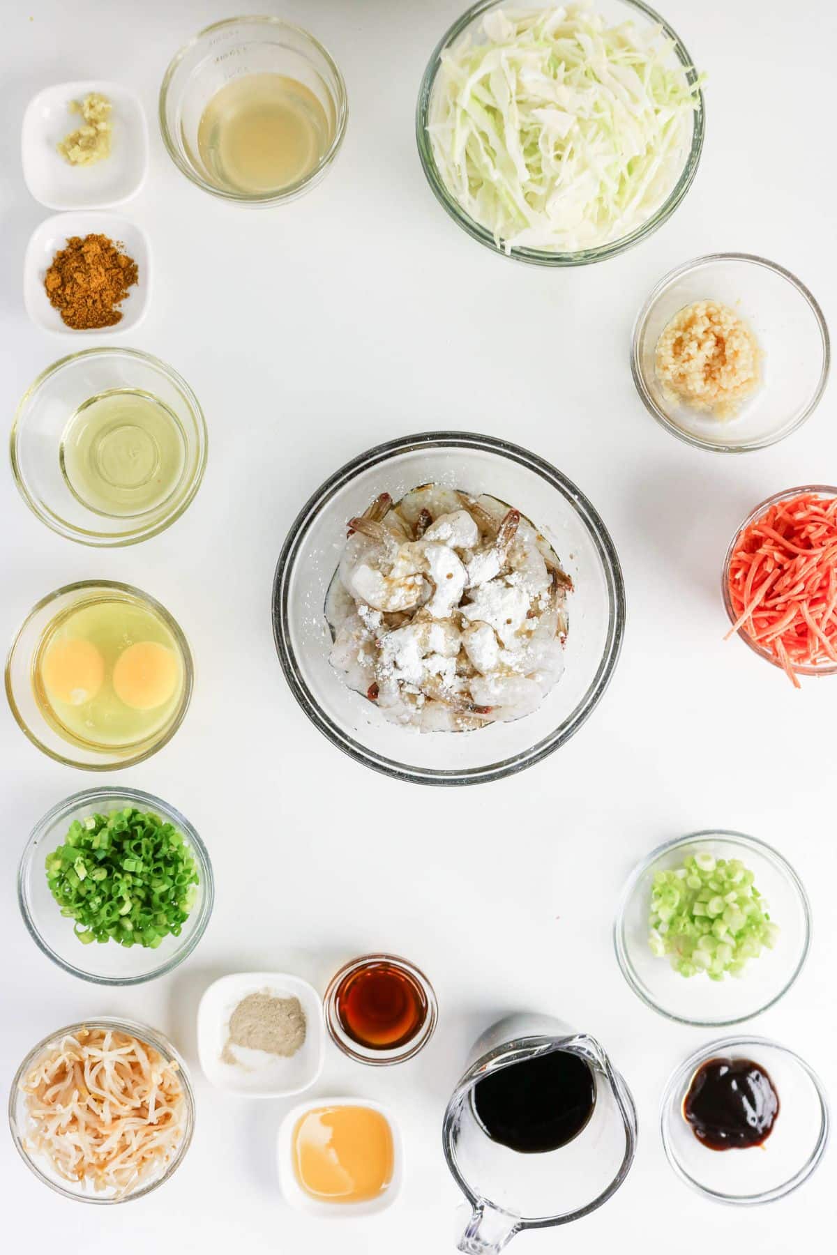 Bowls of shrimp, eggs, chopped veggies, sauces, and seasonings arranged on a white surface for cooking.