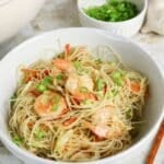 Bowl of shrimp stir-fried noodles with sliced green onions and carrots, with extra green onions in a small bowl.