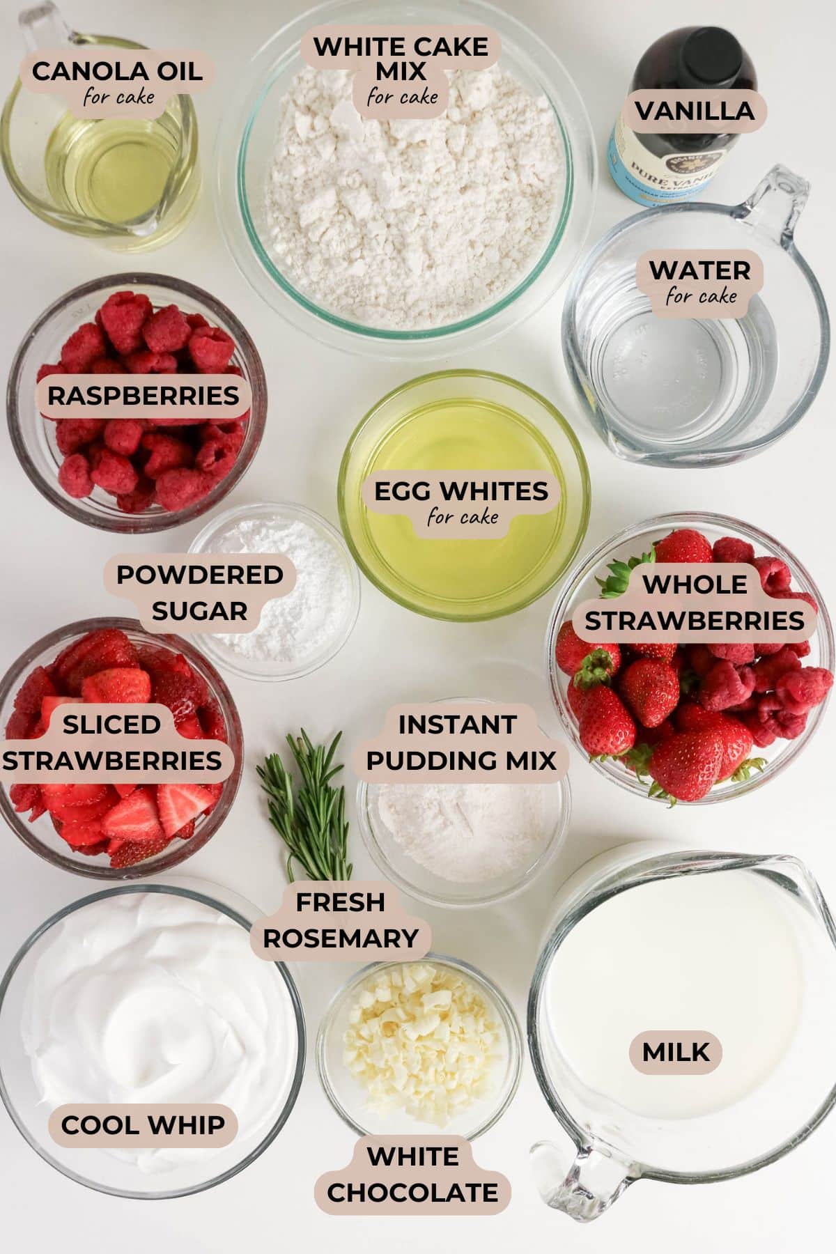 All the trifle ingredients laid out and labeled: cake mix, oil, egg whites, water, pudding mix, milk, whipped topping, berries, white chocolate, rosemary, vanilla, and powdered sugar.