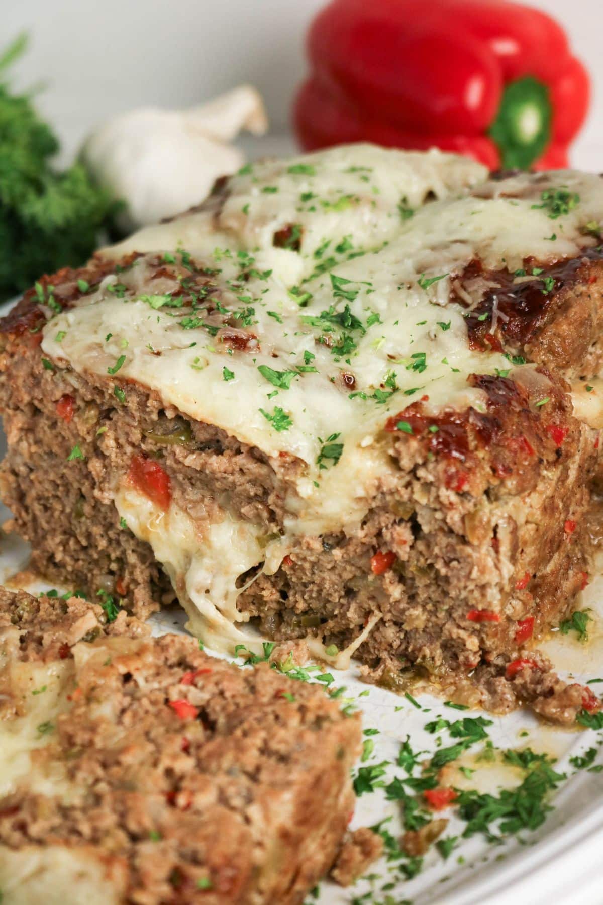 Meatloaf topped with melted cheese and fresh herbs, with a slice cut and set aside.