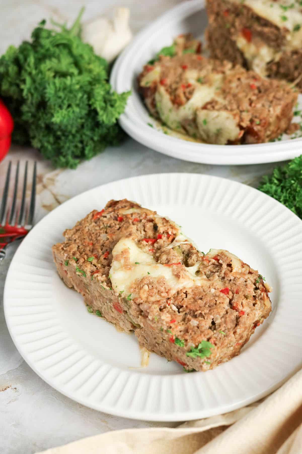 A slice of cheese-topped meatloaf on a white plate.