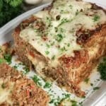 Meatloaf topped with melted cheese and fresh herbs on a platter.